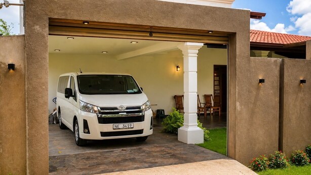A white van parked inside a garage with a stone exterior and a tiled roof. - Luxury 5BR Family Villa Near Airport, Pool, Rooftop, Sleeps 14+ (Pansilgoda)