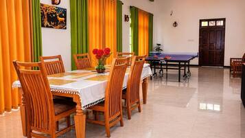 A dining area with a table set for six, chairs, a ping pong table, and a wall with a painting.