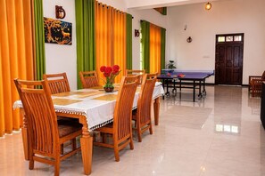 A dining area with a table set for six, chairs, a ping pong table, and a wall with a painting.