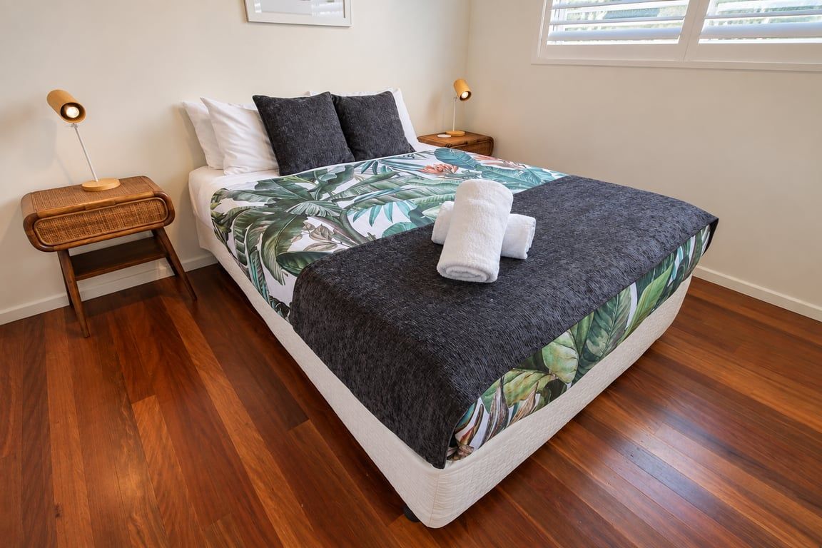 Un lit bien fait, recouvert d’une couvre-lit à motifs tropicaux, avec deux lampes de chevet et une paire de serviettes posées sur le lit.