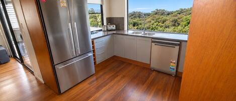 Eine moderne Küche mit einem Edelstahl-Kühlschrank, einem Geschirrspüler und einem Fenster mit Blick auf Grünflächen.