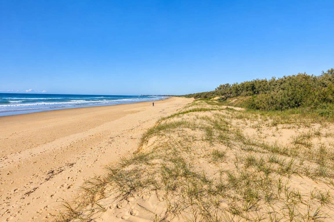 Ein sandiger Strand mit sanften Wellen, einem klaren Himmel und weiter Aussicht auf den Ozean.