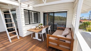 Un patio techado al aire libre con una mesa de madera, sillas blancas, un sofá y una escalera.