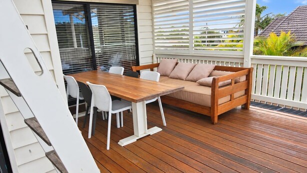 Una terraza de madera con una mesa, sillas, un sofá y una barandilla blanca.