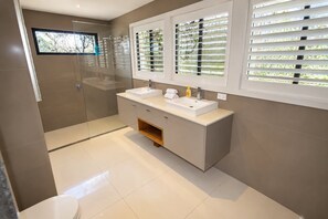 A modern bathroom with a glass shower enclosure, a double sink vanity, and a window with blinds. - Sea Breezes and Sand Between Your Toes (Sunshine Coast)