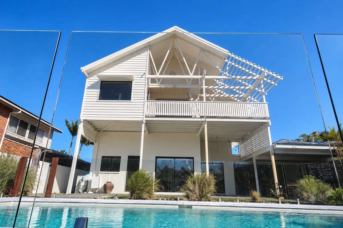 Une maison à deux étages avec un balcon, une piscine et un ciel d’un bleu éclatant.