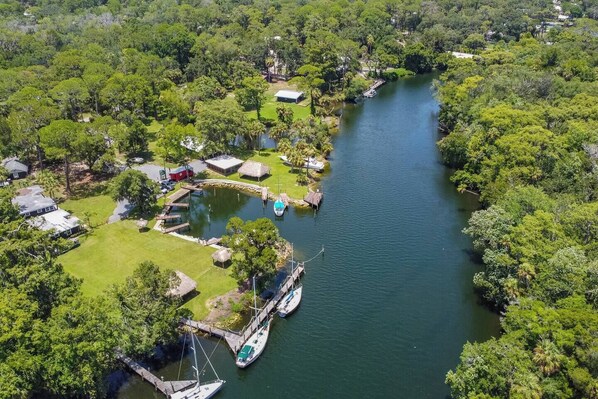 An aerial view of a riverside property with a dock, boats, and a small building.