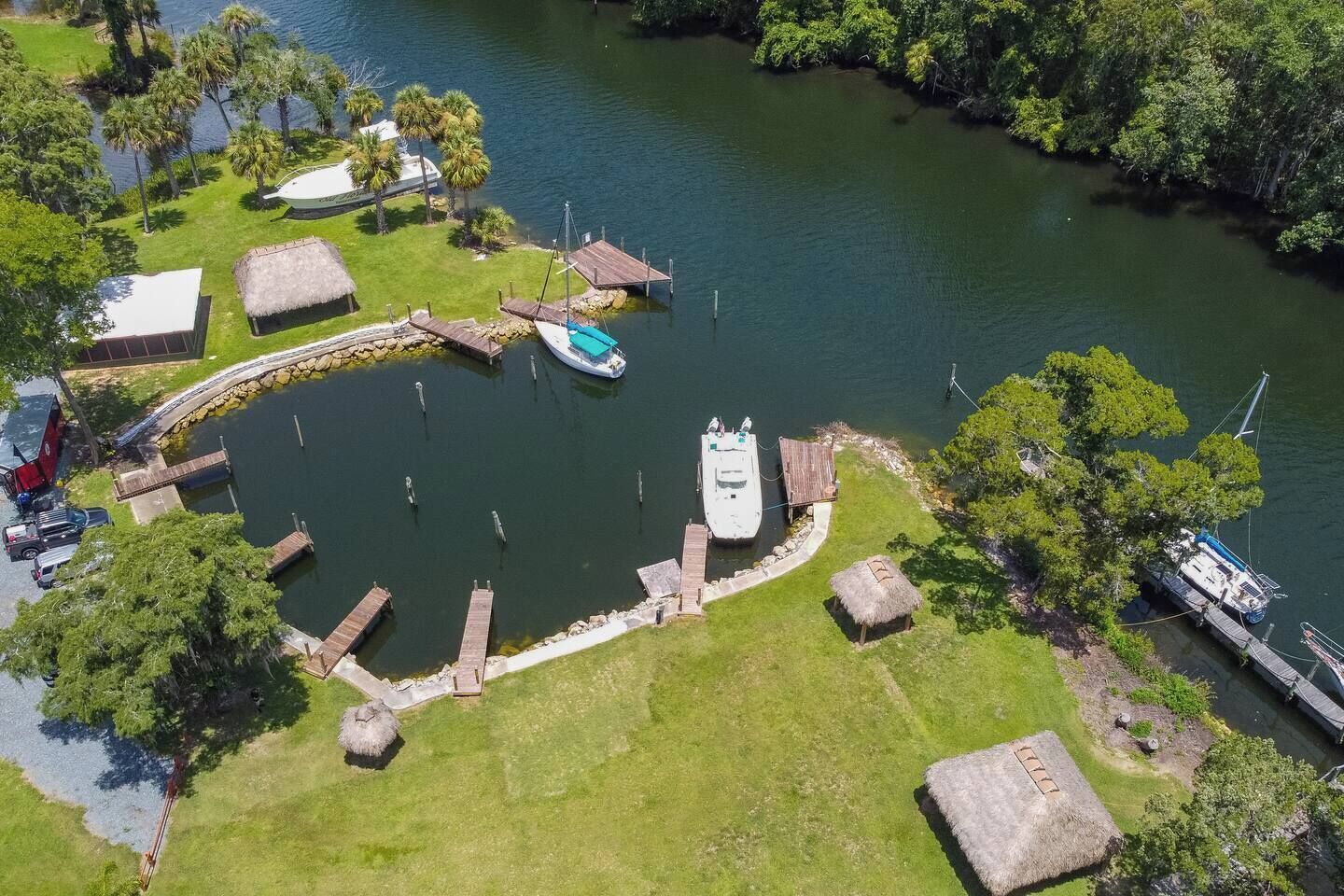Une vue aérienne d’une marina où sont amarrés des bateaux, entourée de verdure et comprenant une petite zone de quai.