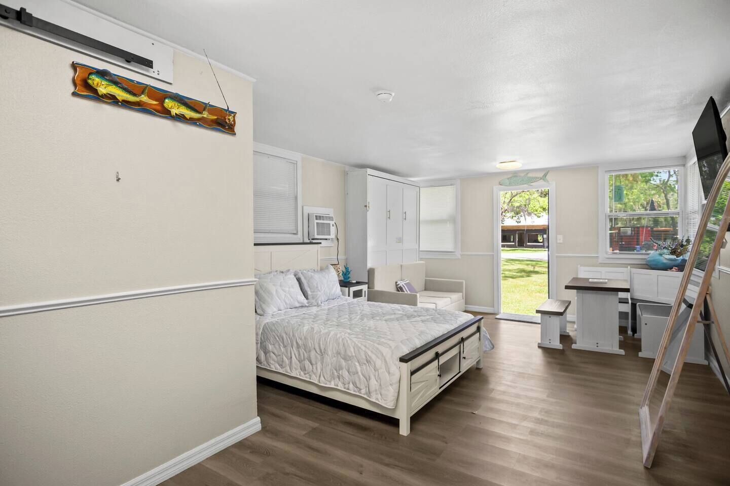 A bedroom with a bed, a desk, and a chair. There is a window with a view of the outdoors.