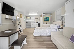 A compact room with a bed, a desk, a TV, a kitchenette, and a bathroom.