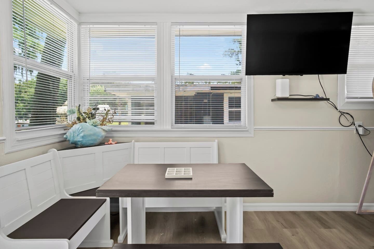 A room with a table, bench, and a TV mounted on the wall.
