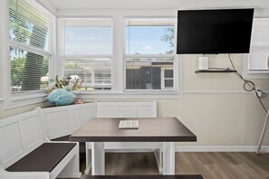 A room with a table, bench, and a TV mounted on the wall.