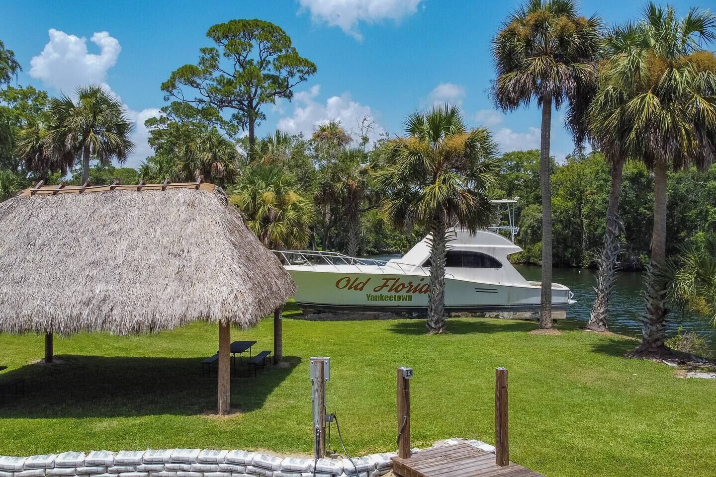 A yacht docked at a marina with a thatched structure nearby.