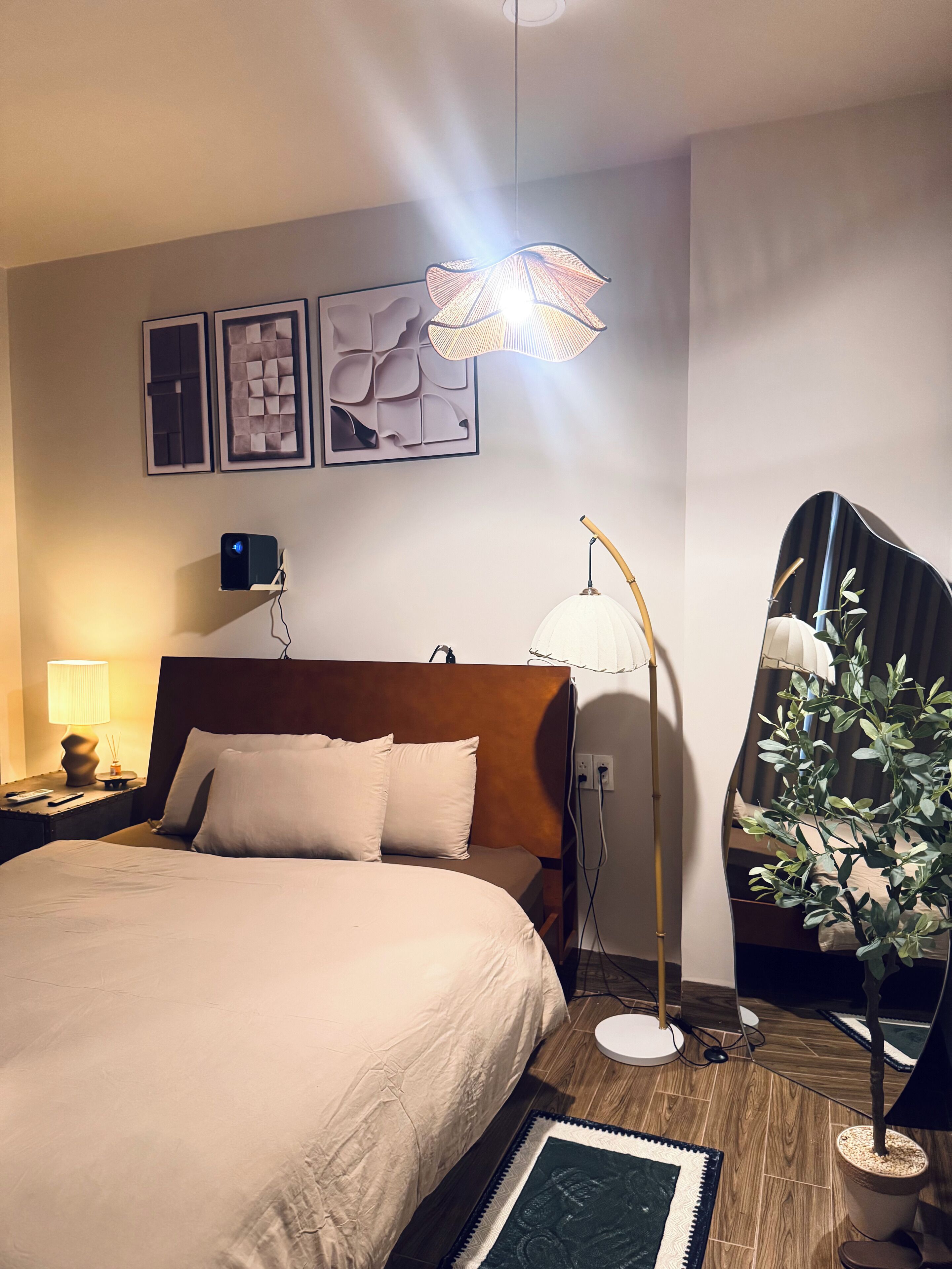 Et hotelværelse med en seng, sengeborde med lamper, en vægmonteret projektor og en potteplante.
