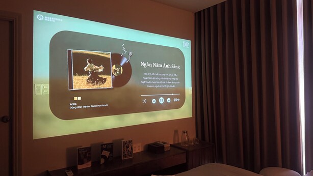 A hotel room with a large screen displaying a music album cover and text. - Ala Homestay Quang Trung (Ho Chi Minh City)