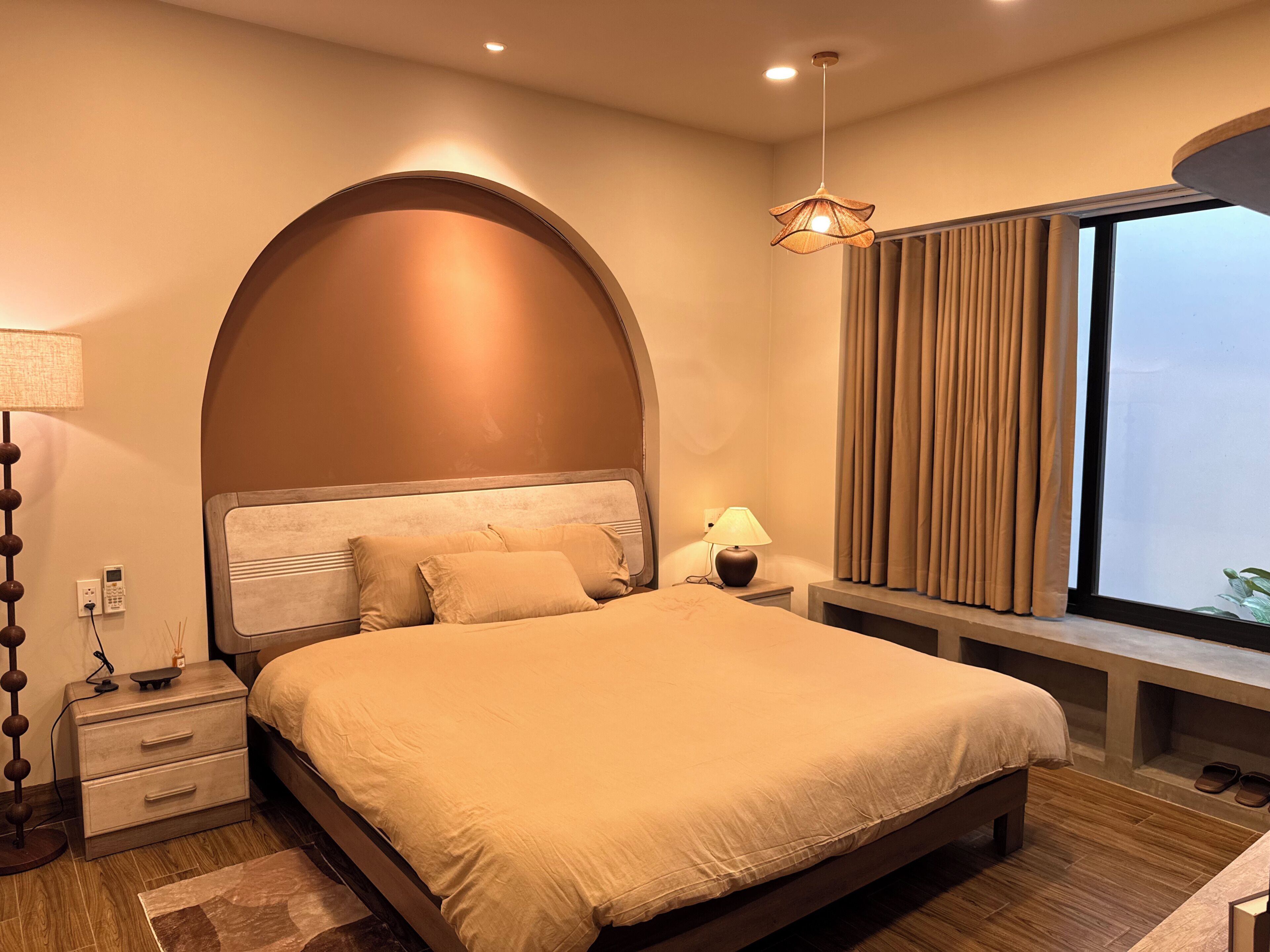 A bedroom with a bed, bedside tables, a lamp, a window with curtains, and a view of the sky.