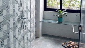 A bathroom with patterned tiles, a shower, a window with a view of trees, and a potted plant on a shelf. - Ala Homestay Quang Trung (Ho Chi Minh City)
