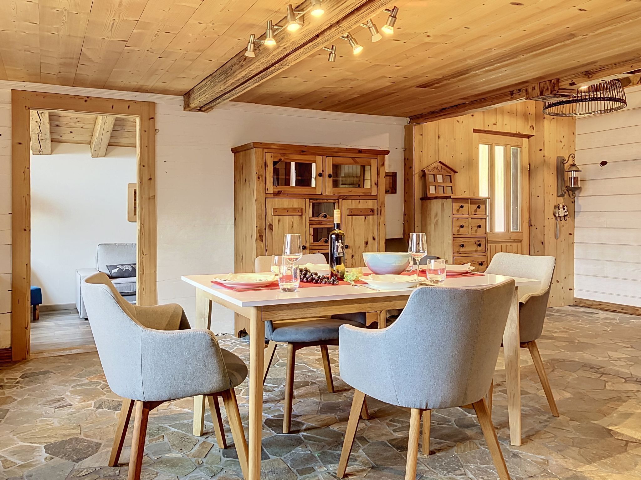 Ein Essbereich mit einem Holztisch, gedeckt für vier Personen, Steinböden und einer rustikalen Küche im Hintergrund.