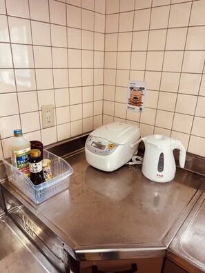 A kitchen counter with a rice cooker, a kettle, and a basket of condiments.