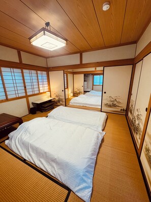 A traditional Japanese-style room with tatami flooring, a futon bed, sliding doors, and a ceiling fan.
