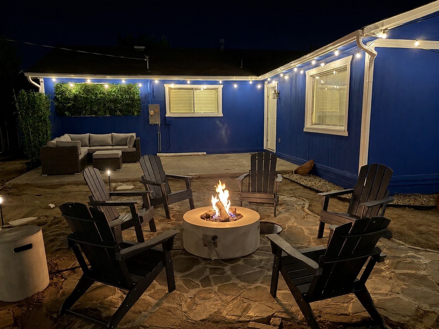 An outdoor patio area with a stone floor, a fire pit, and several Adirondack chairs.