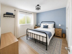 A bedroom with a bed, bedside tables, a nightstand, a hanging light fixture, a window with curtains, and a wooden dresser. - Biggest Little Blue House - near restaurants, casinos, airport, heart of Reno (Reno)