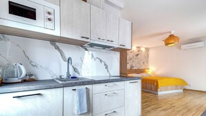 Una cucina moderna con forno a microonde integrato, un lavello con rubinetto e un bollitore. Si vede un letto con una coperta gialla e una parete alle spalle con un motivo geometrico.