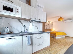 A modern kitchen with a built-in microwave, a sink with a faucet, and a kettle. There is a bed with a yellow blanket and a geometric-patterned wall behind it. - Apartament nr 24 by Interhome (Gliwice)