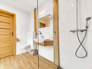 Ein modernes Badezimmer mit Holztür, Toilette, Waschbecken und Dusche mit Duschbrause.