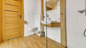 Un bagno moderno con porta in legno, piastrelle bianche, box doccia in vetro e lavandino bianco.