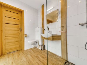 A modern bathroom with a wooden door, white tiles, a glass shower enclosure, and a white sink. - Apartament nr 24 by Interhome (Gliwice)
