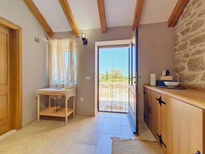 Una habitación con un armario de madera, una mesita con un tazón, una puerta que da al exterior y una pared de piedra.