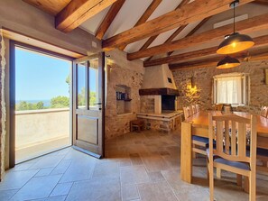 Ein rustikales Interieur mit Kamin aus Stein, Esstisch aus Holz und Blick durch eine Glastür.
