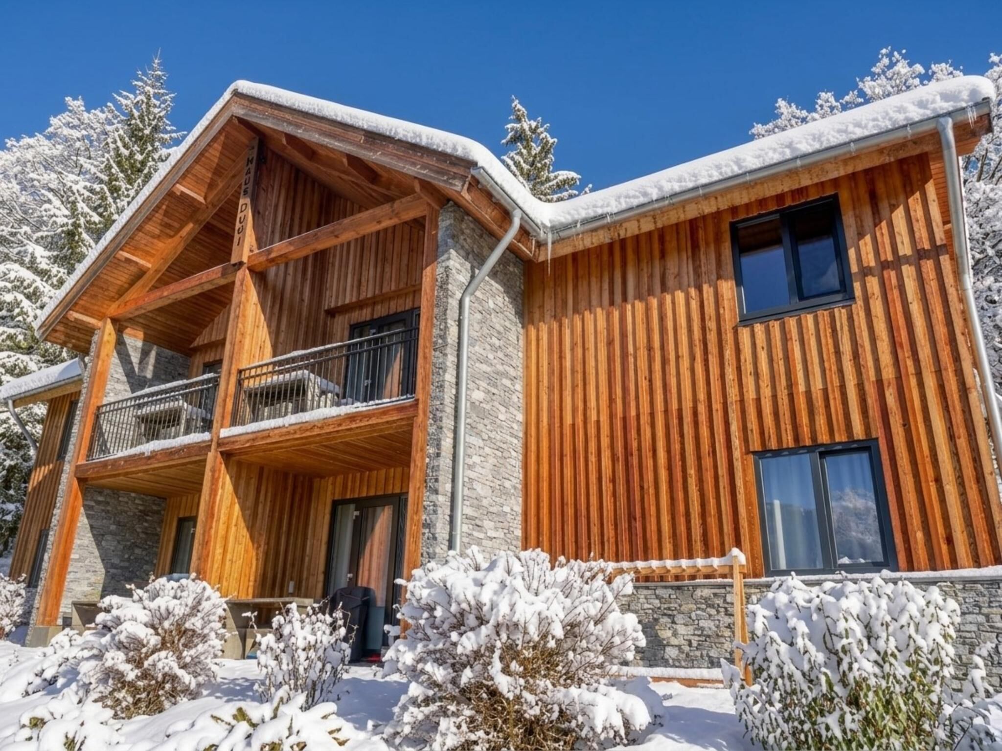 A two-story wooden cabin with a balcony, surrounded by snow-covered trees.
