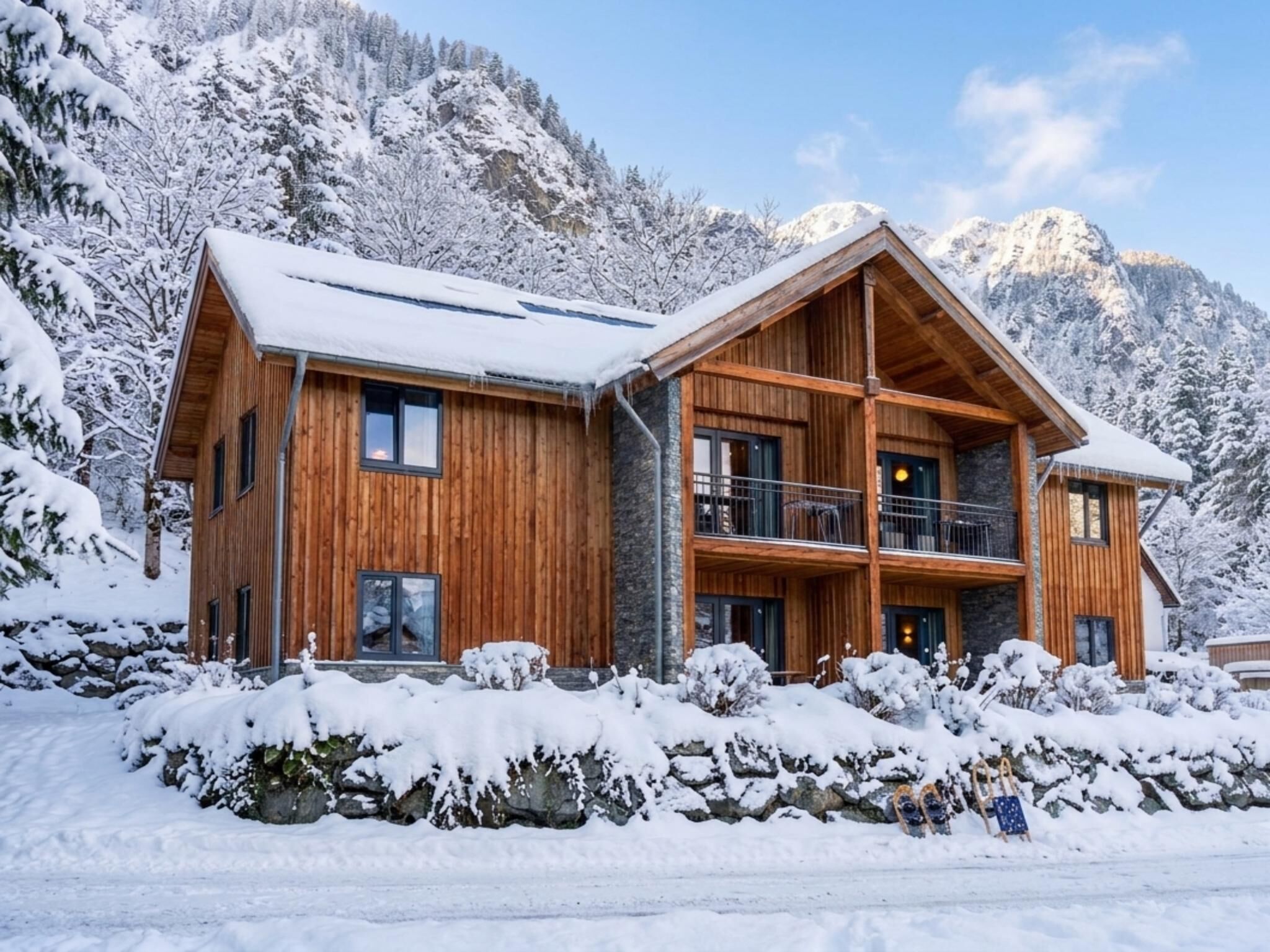 Un chalet de madera de dos pisos con un balcón, frente a un paisaje montañoso nevado.