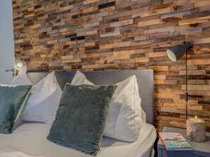 Ein Bett mit Kissen, ein Nachttisch mit Lampe und eine Wand mit Holzpaneelen.