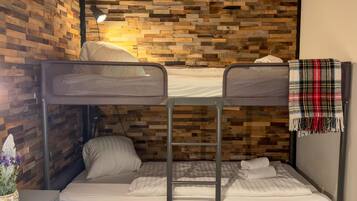 A bunk bed room with a wooden wall, a desk with a lamp, and a plaid blanket on the right.