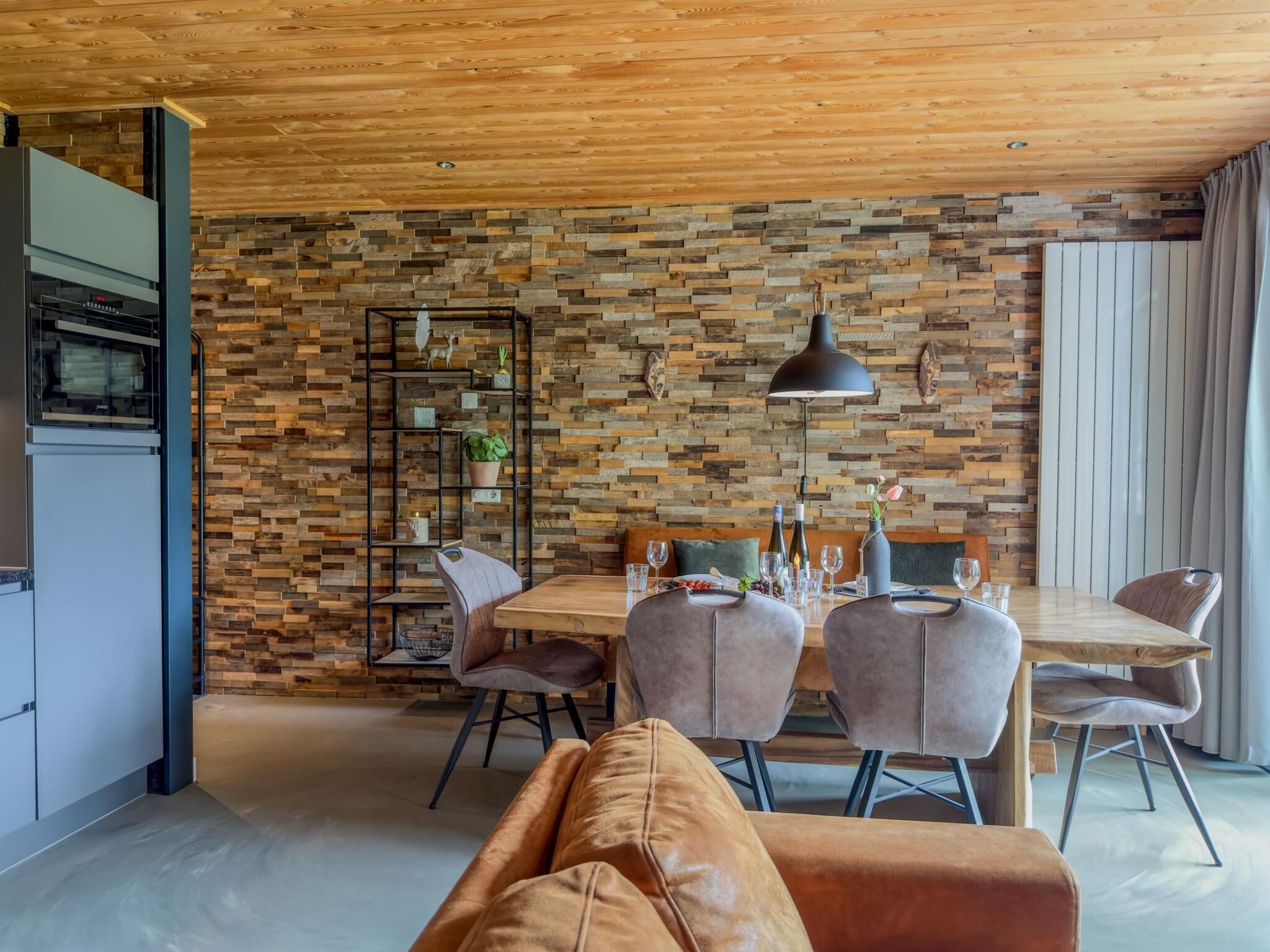 A modern dining area with a wooden wall, a dining table set for four, and a sofa in the foreground.