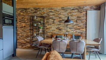 A modern dining area with a wooden wall, a dining table set for four, and a sofa in the foreground.