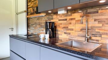 A modern kitchen with a black countertop, stainless steel sink, and a coffee maker.