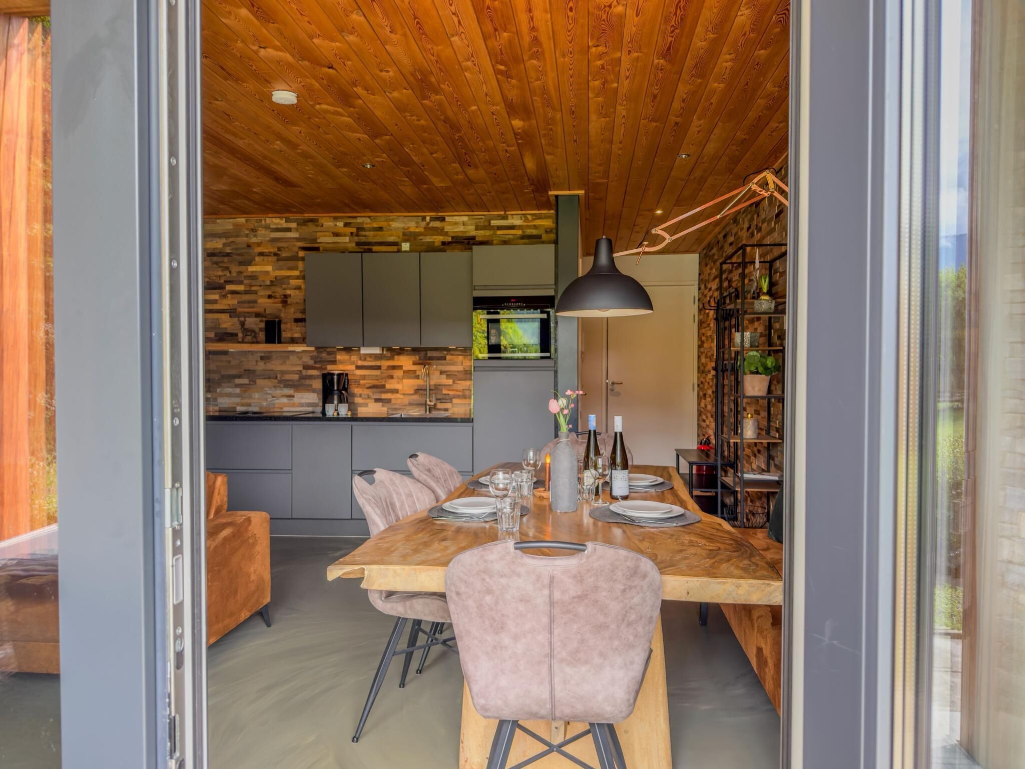 A modern dining area with a wooden table, chairs, and a kitchen in the background.