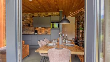 A modern dining area with a wooden table, chairs, and a kitchen in the background.