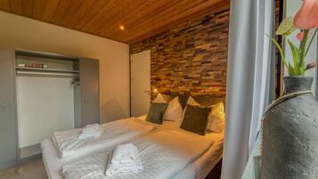 A hotel room with a wooden ceiling, a bed with white linens, a stone wall, and a vase with flowers.