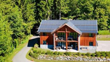 Une cabane en bois à deux étages, surmontée d’un toit en métal, et entourée d’une végétation luxuriante.