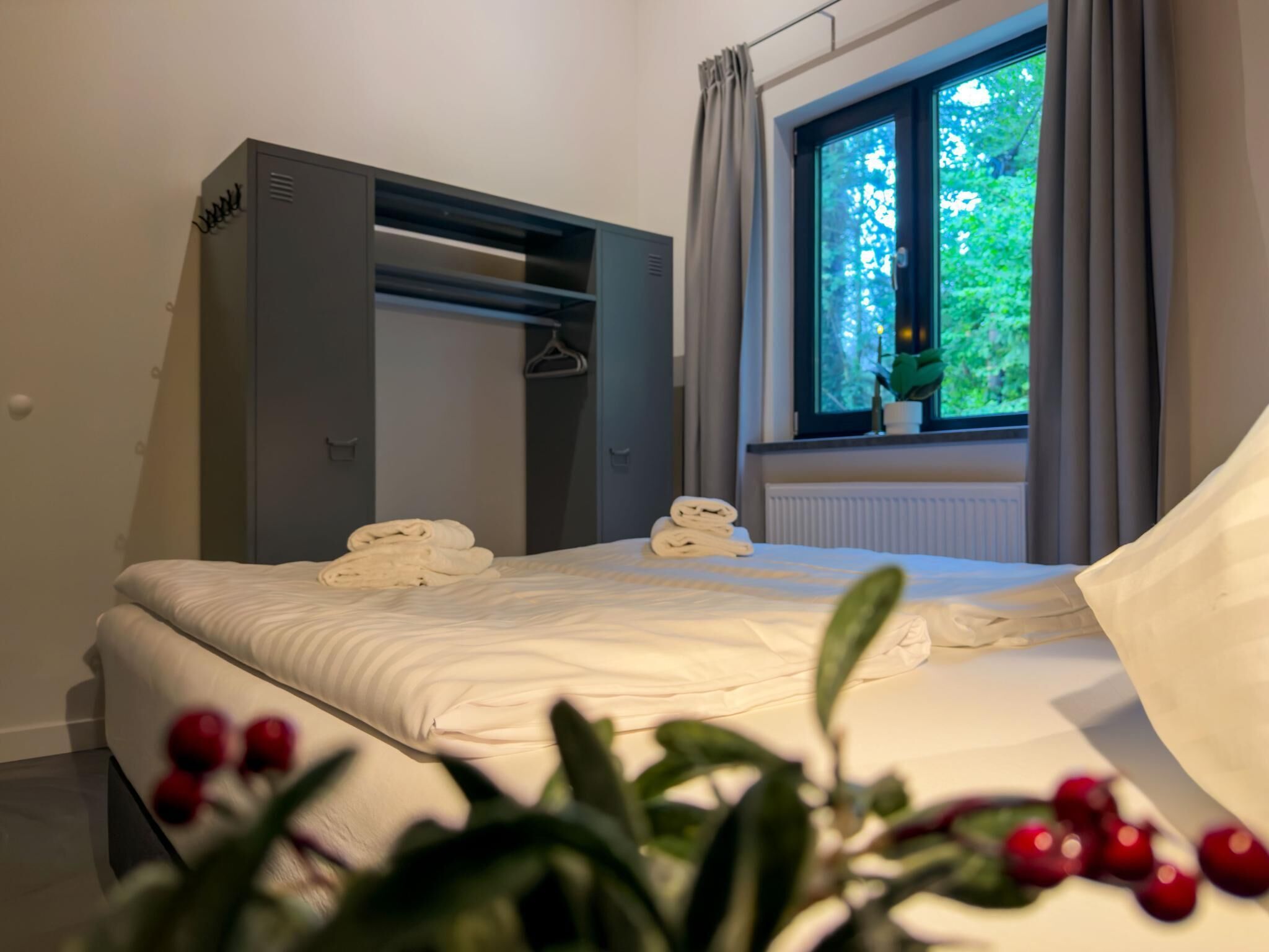 A bedroom with a bed, a wardrobe, a window with curtains, and a potted plant.