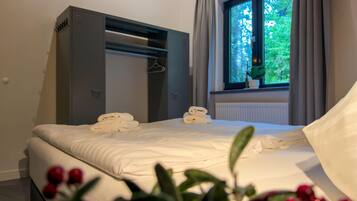 A bedroom with a bed, a wardrobe, a window with curtains, and a potted plant.