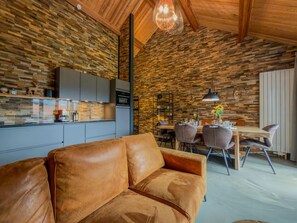 A modern interior with a stone wall, a leather sofa, and a dining area with chairs and a table. - Cozy holiday apartment by a lake in Carinthia (Hermagor-Pressegger See)