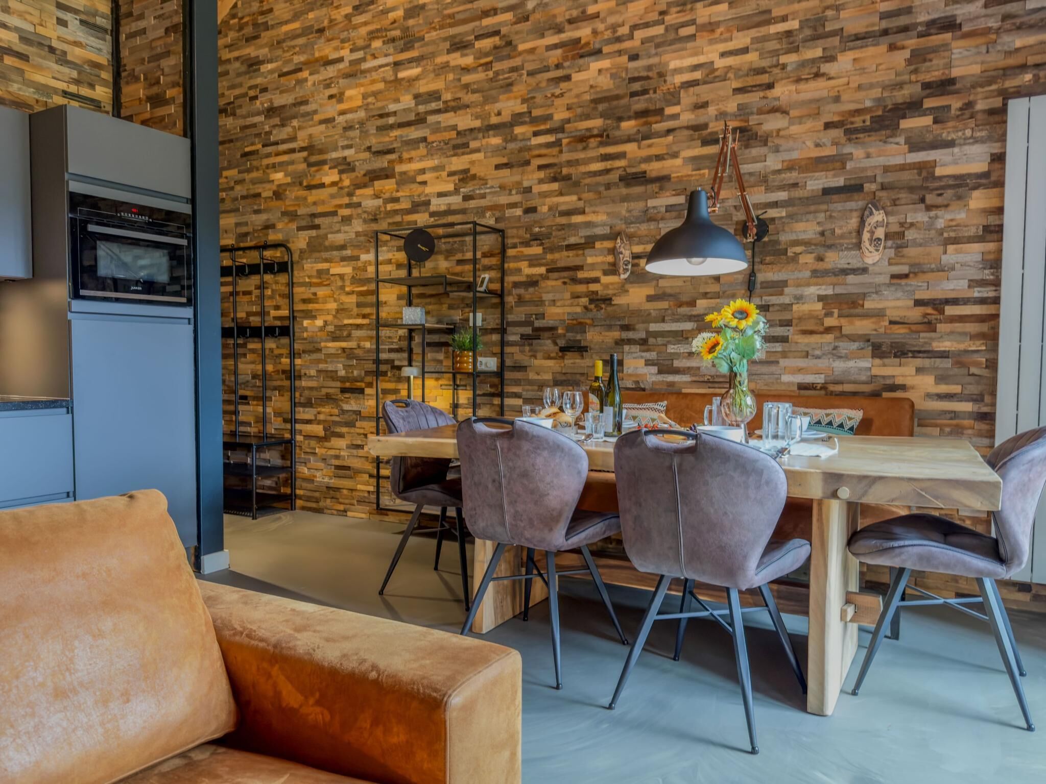 A modern kitchen with a wooden wall, a dining table with chairs, and a sofa.