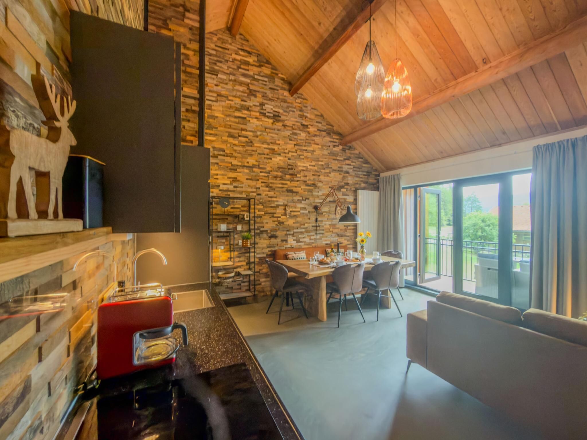 A modern kitchen with a stone wall, a dining area with a table and chairs, and a large window with a view.