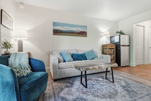 A living room with a sofa, a coffee table, a rug, a painting, and a refrigerator. - Cozy Condo by Downtown (Bend)